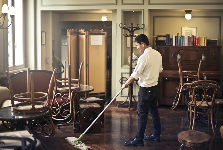 A worker cleaning a restaurant at night, with chairs stacked on tables, emphasizing nightly restaurant cleaning services.