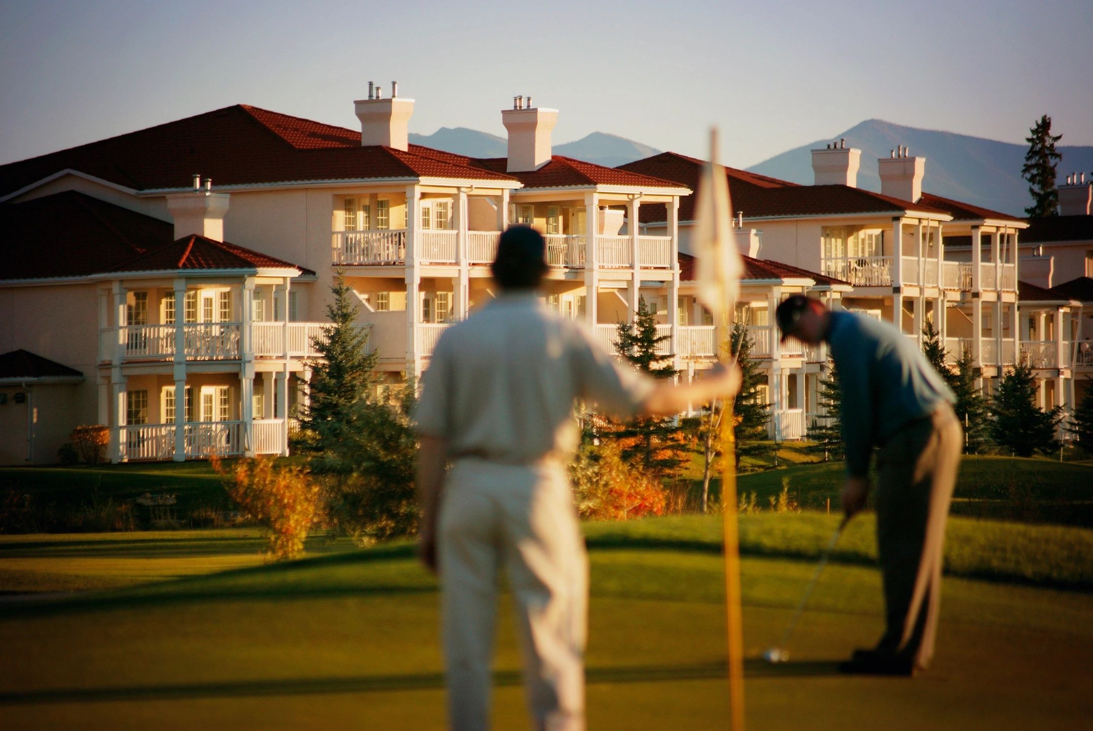 Two golfers on a clean, well-maintained course in front of a beautiful resort with spotless buildings.