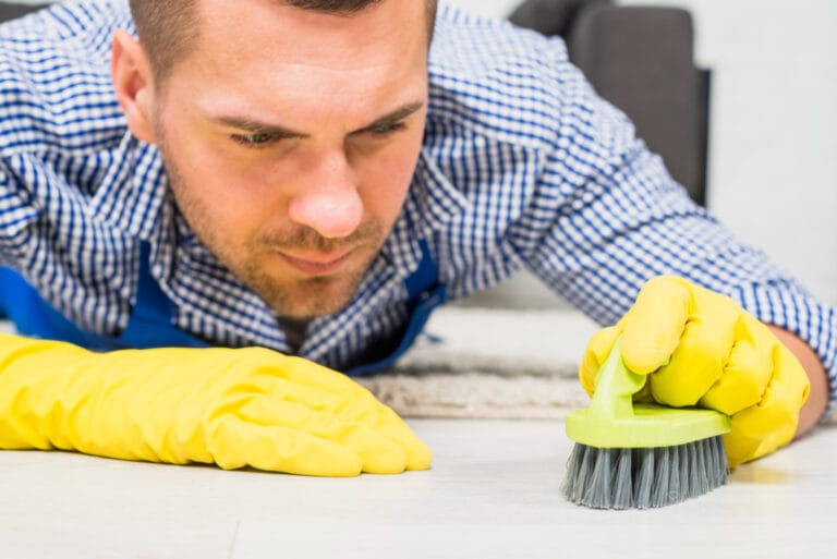 Close-up of a professional cleaner focusing on grout lines with a small brush for detailed cleaning.